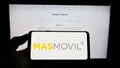 Person holding smartphone with logo of Spanish MÃÂ¡sMÃÂ³vil Ibercom S.A. (Grupo MasMovil) on screen in front of website. Royalty Free Stock Photo