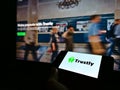 Person holding smartphone with logo of Swedish fintech company Trustly Group on screen in front of website.