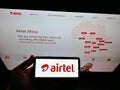 Person holding smartphone with logo of telecommunications provider Airtel Africa plc on display in front of website.