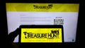 Person holding smartphone with logo of The Treasure Hunt Company (Brighton) on screen in front of website.