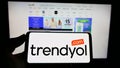 Person holding smartphone with logo of Turkish e-commerce company Trendyol on screen in front of website.