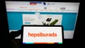Person holding smartphone with logo of Turkish e-commerce platform Hepsiburada on screen in front of website.