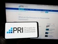 Person holding smartphone with logo of UN Principles for Responsible Investment (PRI) on screen in front of website.