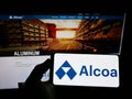 Person holding smartphone with logo of US aluminium company Alcoa Corporation on screen in front of website.