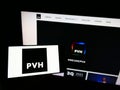 Person holding smartphone with logo of US clothing company PVH Corp. on screen in front of website.