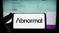 Person holding smartphone with logo of US company Abnormal Security Corp. on screen in front of website.