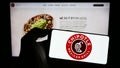 Person holding smartphone with logo of US company Chipotle Mexican Grill Inc. on screen in front of website.