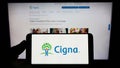 Person holding smartphone with logo of US company Cigna Corporation on screen in front of website.