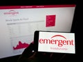 Person holding smartphone with logo of US company Emergent BioSolutions Inc. on screen in front of website.