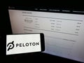Person holding smartphone with logo of US company Peloton Interactive Inc. on screen in front of website.