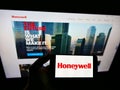 Person holding smartphone with logo of US conglomerate Honeywell International Inc. on screen in front of website.