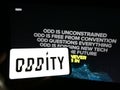Person holding smartphone with logo of US consumer technology company Oddity Inc. on screen in front of website.