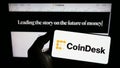 Person holding smartphone with logo of US crypto news company CoinDesk Inc. on screen in front of website. Royalty Free Stock Photo