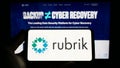 Person holding smartphone with logo of US data security company Rubrik Inc. on screen in front of website.