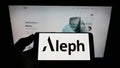 Person holding smartphone with logo of US digital media company Aleph Holding on screen in front of website.