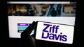 Person holding smartphone with logo of US digital media company Ziff Davis Inc. on screen in front of website.