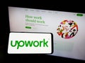 Person holding smartphone with logo of US freelancing platform Upwork Global Inc. on screen in front of website. Royalty Free Stock Photo