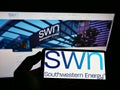 Person holding smartphone with logo of US gas company Southwestern Energy Co. (SWN) on screen in front of website. Royalty Free Stock Photo