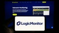 Person holding smartphone with logo of US monitoring company LogicMonitor Inc. on screen in front of website.