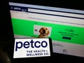 Person holding smartphone with logo of US pet retailer Petco Health and Wellness Company Inc. on screen in front of website.