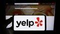 Person holding smartphone with logo of US review platform company Yelp Inc. on screen in front of website.