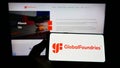 Person holding smartphone with logo of US semiconductor company GlobalFoundries Inc. (GF) on screen in front of website.