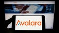 Person holding smartphone with logo of US software company Avalara Inc. on screen in front of website.