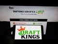 Person holding smartphone with logo of US sports betting company DraftKings Inc. on screen in front of website.