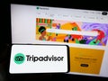Person holding smartphone with logo of US travel company Tripadvisor Inc. on screen in front of website.