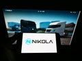Person holding smartphone with logo of US zero-emission vehicle company Nikola Corporation on screen in front of web page.