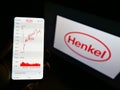 Person holding smartphone with stock price chart of German chemical and consumer goods company Henkel on display with logo. Royalty Free Stock Photo