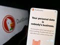 Person holding smartphone with web page of Internet search engine DuckDuckGo (DDG) on screen in front of logo.