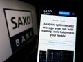 Person holding smartphone with webpage of Danish investment banking company Saxo Bank AS on screen with logo. Royalty Free Stock Photo