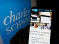 Person holding smartphone with webpage of financial company The Charles Schwab Corporation on screen with logo.