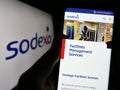 Person holding smartphone with webpage of French facility management company Sodexo S.A. on screen with logo.