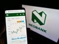 Person holding smartphone with webpage with stock chart of South African bank Nedbank Group Ltd on screen in front of logo.