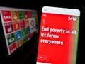 Person holding smartphone with webpage of UN Sustainable Development Goals (SDG) on screen in front of logo.