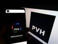 Person holding smartphone with website of American clothing company PVH Corp. on screen in front of logo.