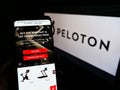 Person holding smartphone with website of American company Peloton Interactive Inc. on screen in front of logo.