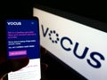 Person holding smartphone with website of Australian telco company Vocus Group Limited on screen in front of logo.