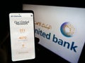 Person holding smartphone with website of Bahraini company Ahli United Bank (AUB) on screen in front of logo.