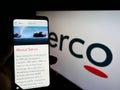 Person holding smartphone with website of British service company Serco Group plc on screen in front of logo.