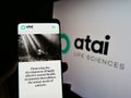 Person holding smartphone with website of German biotech company ATAI Life Sciences AG on screen in front of logo..