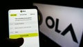 Person holding smartphone with website of Indian ridesharing company Ola Cabs on screen in front of business logo.