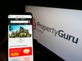 Person holding smartphone with website of online property company PropertyGuru Pte. Ltd. on screen with logo.