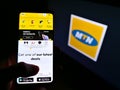 Person holding smartphone with website of South African telecommunications provider MTN Group on screen in front of logo. Royalty Free Stock Photo