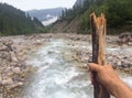 Person holding a stick near a water stream with a blurred nature in the background