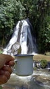 Person holding a traditional tea or coffee cup in hand against outdoor waterfall. Vertical composition Royalty Free Stock Photo