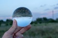 Person holding a transparent sphere in hand in a field during the daytime