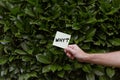 A person holding a white card with a Why? print with the background of green Bay laurels